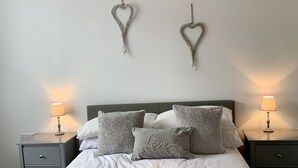 Et soveværelse med en seng, to sengeborde, et blødt vægophæng og hjerteformede dekorationer.