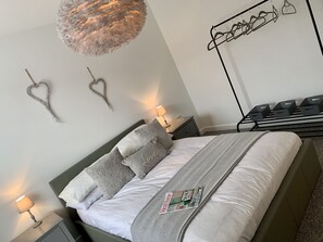 Een keurig opgemaakt slaapkamer met een bed, nachtkastjes, een hanglamp en een wandrek met manden.