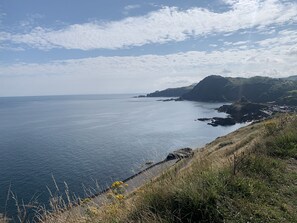 Een kustlandschap met een helder uitzicht op de zee, een rotsachtige kustlijn en een groene heuvel.