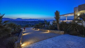 A paved pathway leading to a modern building with a pool area, surrounded by palm trees and a view of distant mountains. - Cozy home in Partinico (Partinico)