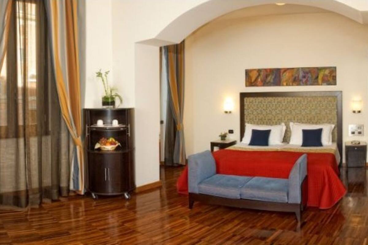 Quarto de hotel com uma cama grande, um sofá, uma mesinha e uma planta decorativa.