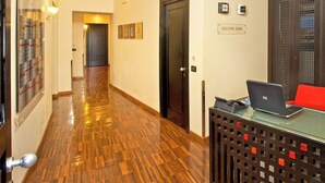 Un espace d’accueil d’hôtel avec un plancher en bois, un comptoir de réception doté d’un ordinateur portable, un fauteuil rouge et un panneau indiquant l’étage réservé aux clients privilégiés.