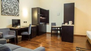 Une chambre d’hôtel compacte avec un plancher en bois, un bureau avec une chaise, un canapé, une petite table avec une chaise et un lit.