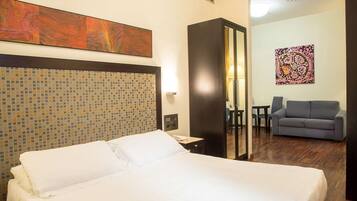 A hotel room with a large bed, a sofa, a desk, and a mirror.