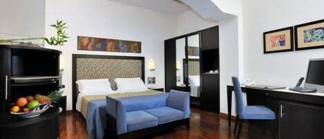 Una habitación de hotel con cama, sofá azul, escritorio y televisor.
