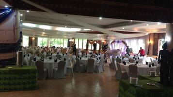 A banquet hall with round tables, chairs, and a stage.