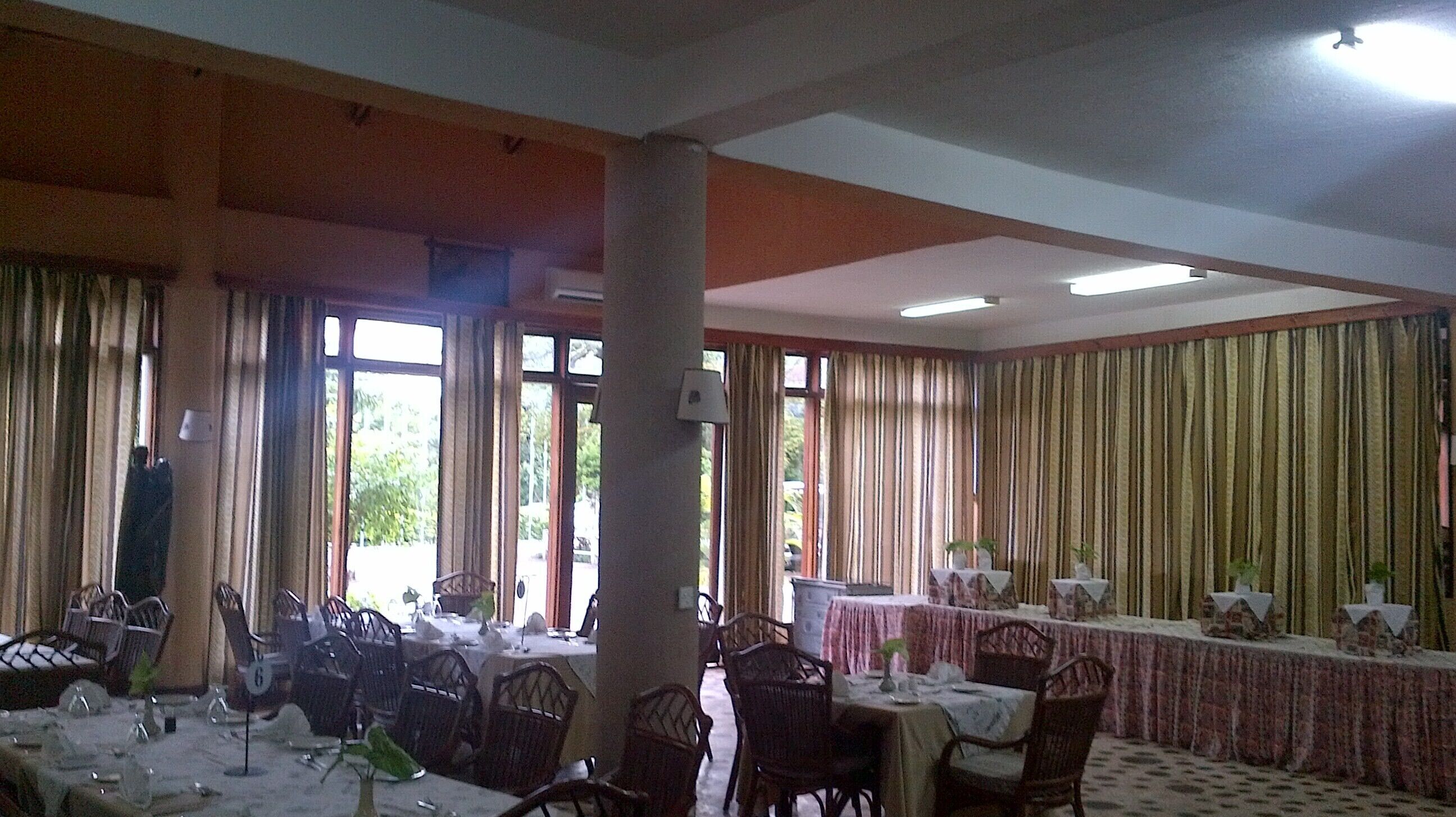 A dining area with tables set for a meal, chairs, and a large window with curtains.