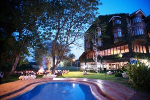 A large building with a swimming pool, surrounded by trees and a well-lit outdoor area. - Ngurdoto Mountain lodge (Arusha)
