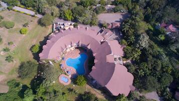 An aerial view of a resort with a central swimming pool, multiple guest villas, and lush greenery surrounding the property.