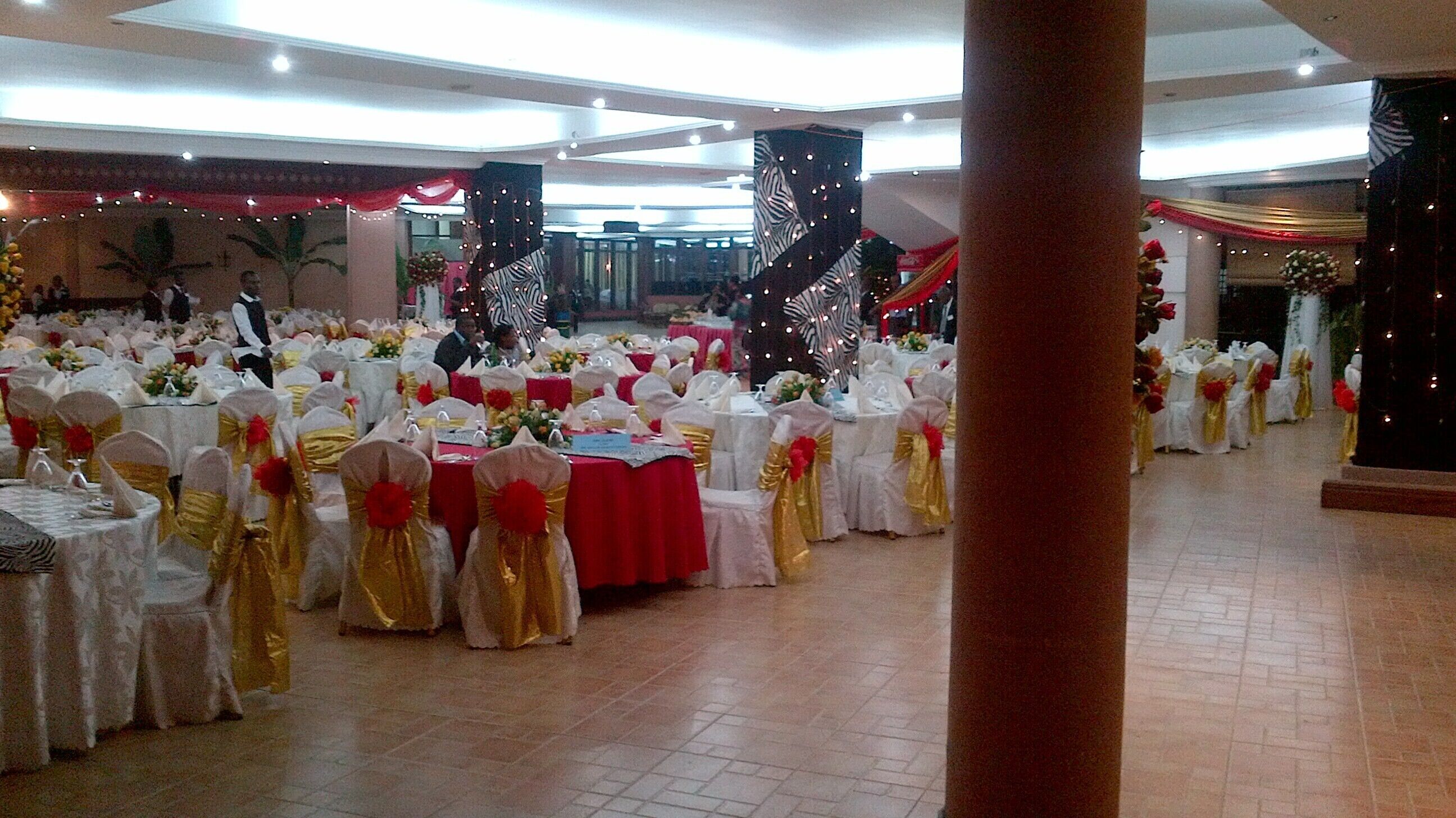Un salón de banquetes con mesas redondas cubiertas con manteles blancos y sillas con cintas doradas.
