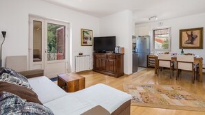 A modern living room with a sofa, a TV, a wooden cabinet, and a dining area with a table and chairs. - 3 bedroom beautiful apartment in Veli Losinj (Veli Losinj)