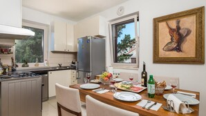 A modern kitchen with a dining area, featuring a large window, a refrigerator, and a dining table set for a meal. - 3 bedroom beautiful apartment in Veli Losinj (Veli Losinj)