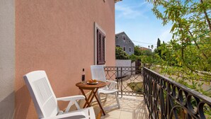 A balcony with white plastic chairs and a small round table, a bottle of alcohol, and a plate of fruit. - 3 bedroom beautiful apartment in Veli Losinj (Veli Losinj)