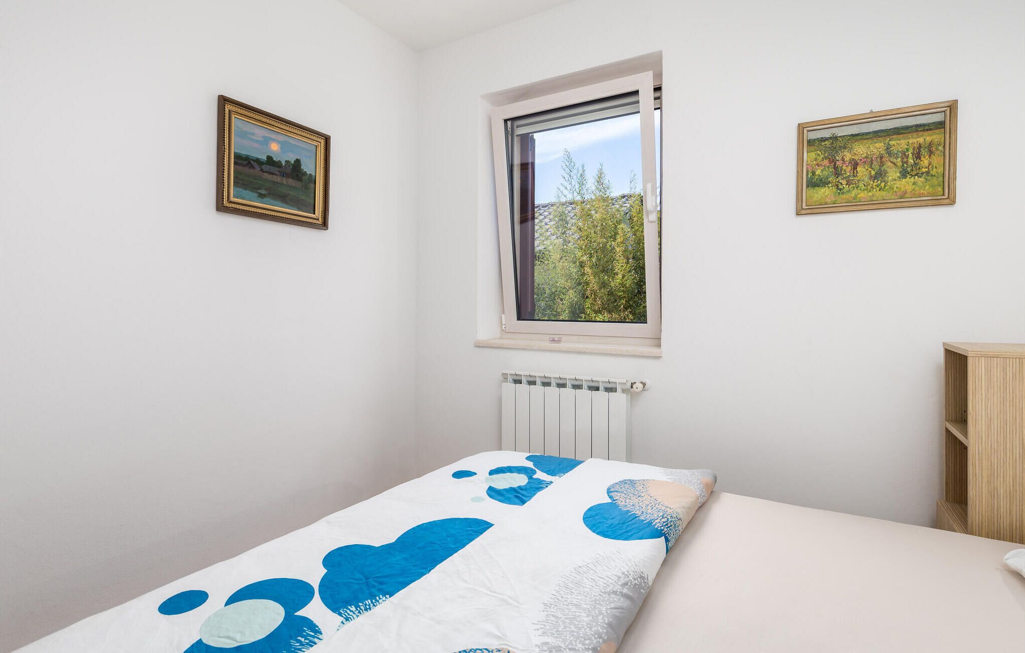 Un dormitorio con una cama, una ventana y dos cuadros en la pared.