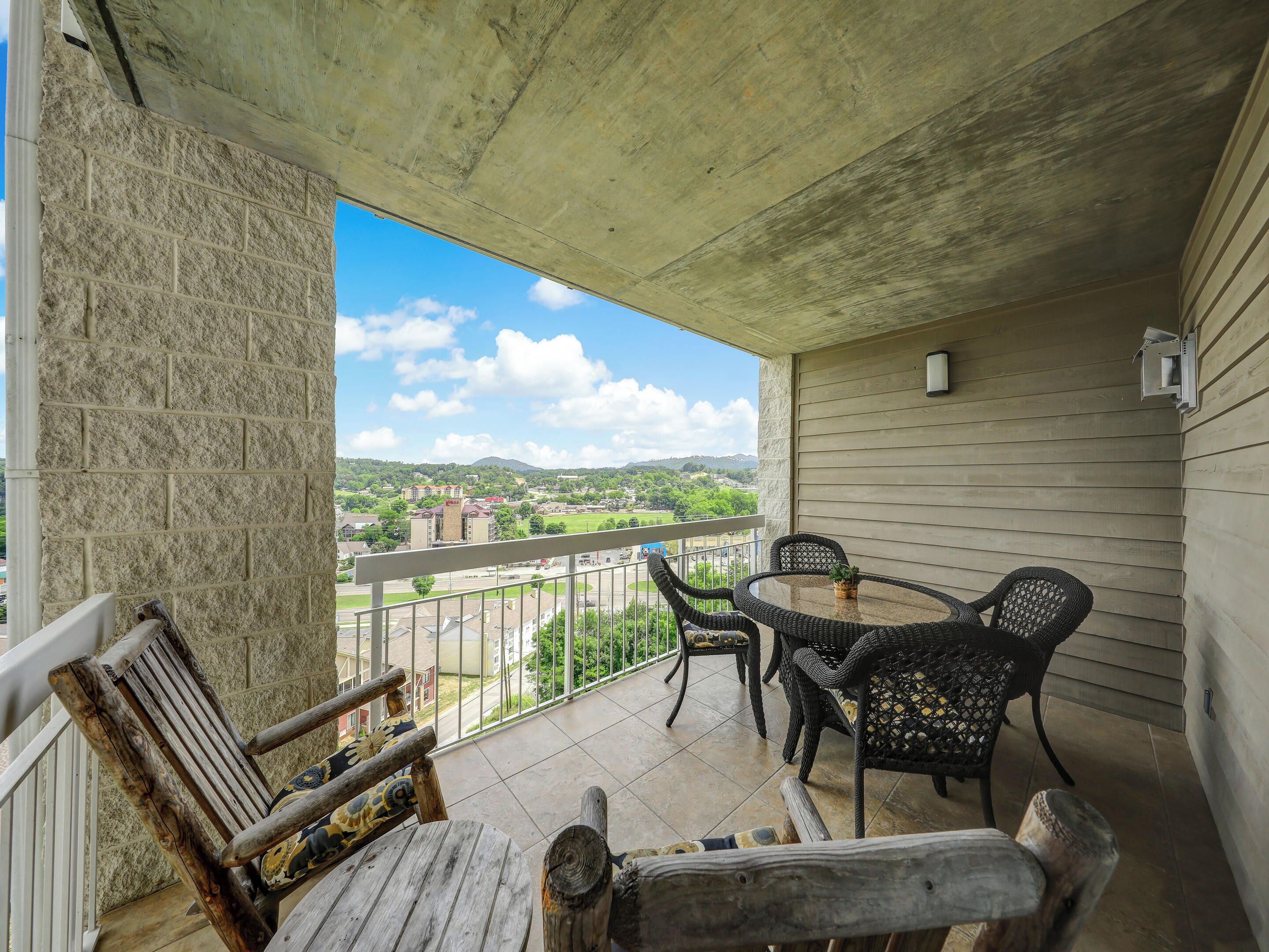 Ein Balkon mit Blick auf eine Stadt, ein runder Tisch mit Stühlen und eine hölzerne Bank.