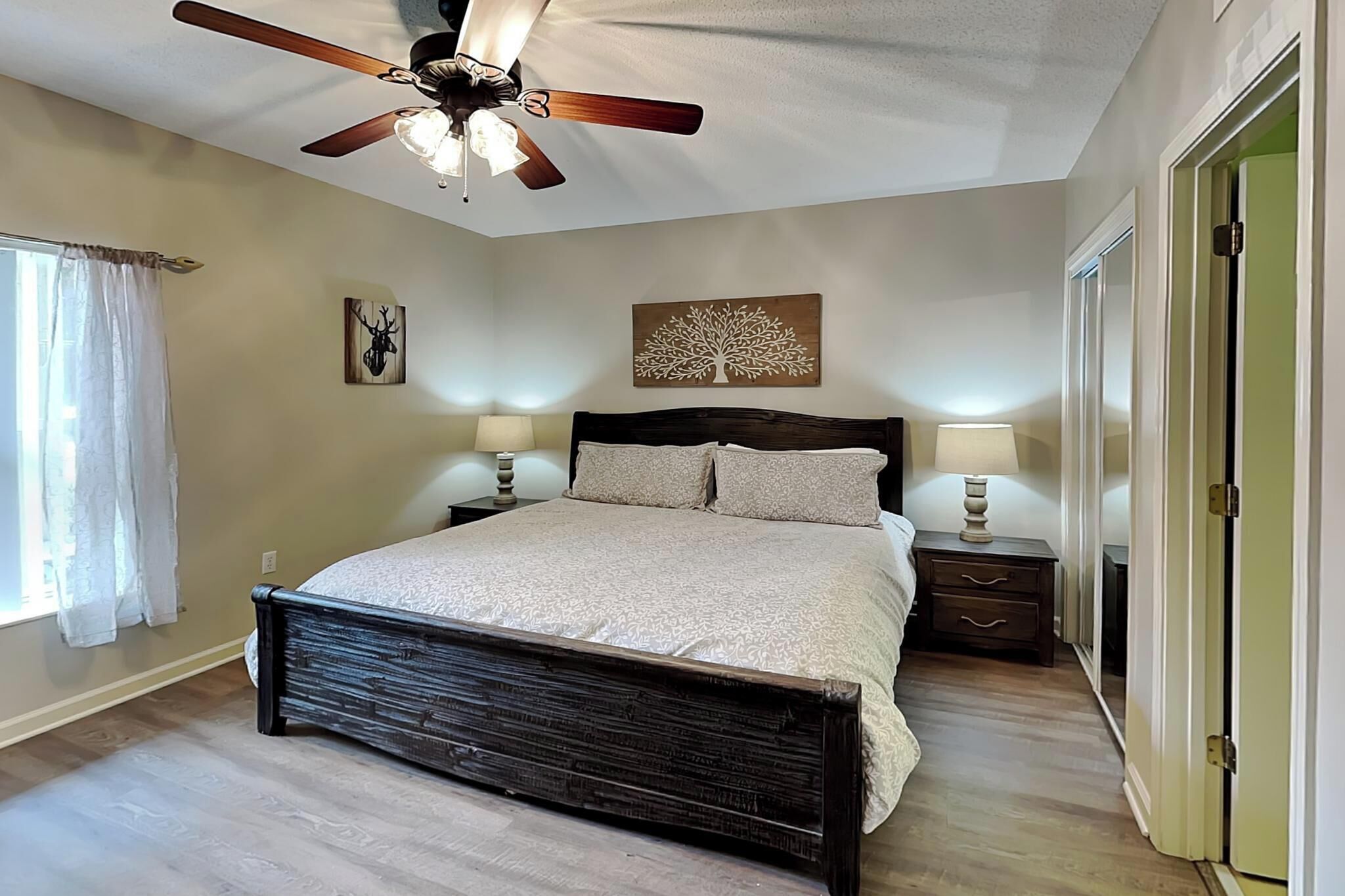 A bedroom with a bed, two bedside tables, a ceiling fan, and a window with curtains.