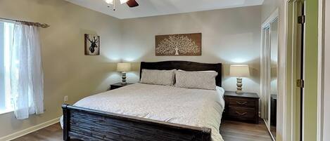 A bedroom with a bed, two bedside tables, a ceiling fan, and a window with curtains.