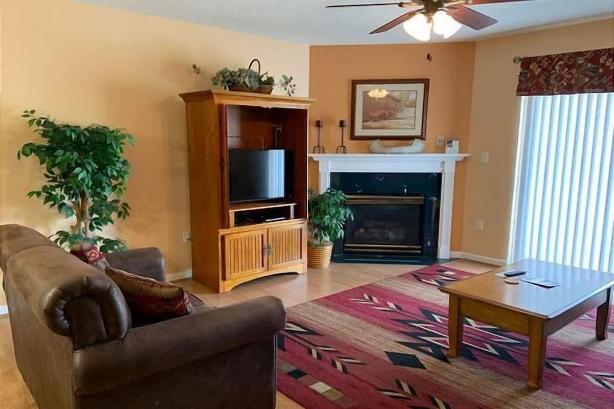 A living room with a sofa, a television on a wooden stand, a fireplace, and a ceiling fan.