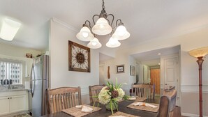 Ein Essbereich mit einem dunklen Holztisch, gedeckt für vier Personen, umgeben von Holzsesseln. Eine Chandelier hängt darüber und ein Blumenstrauß steht auf dem Tisch.