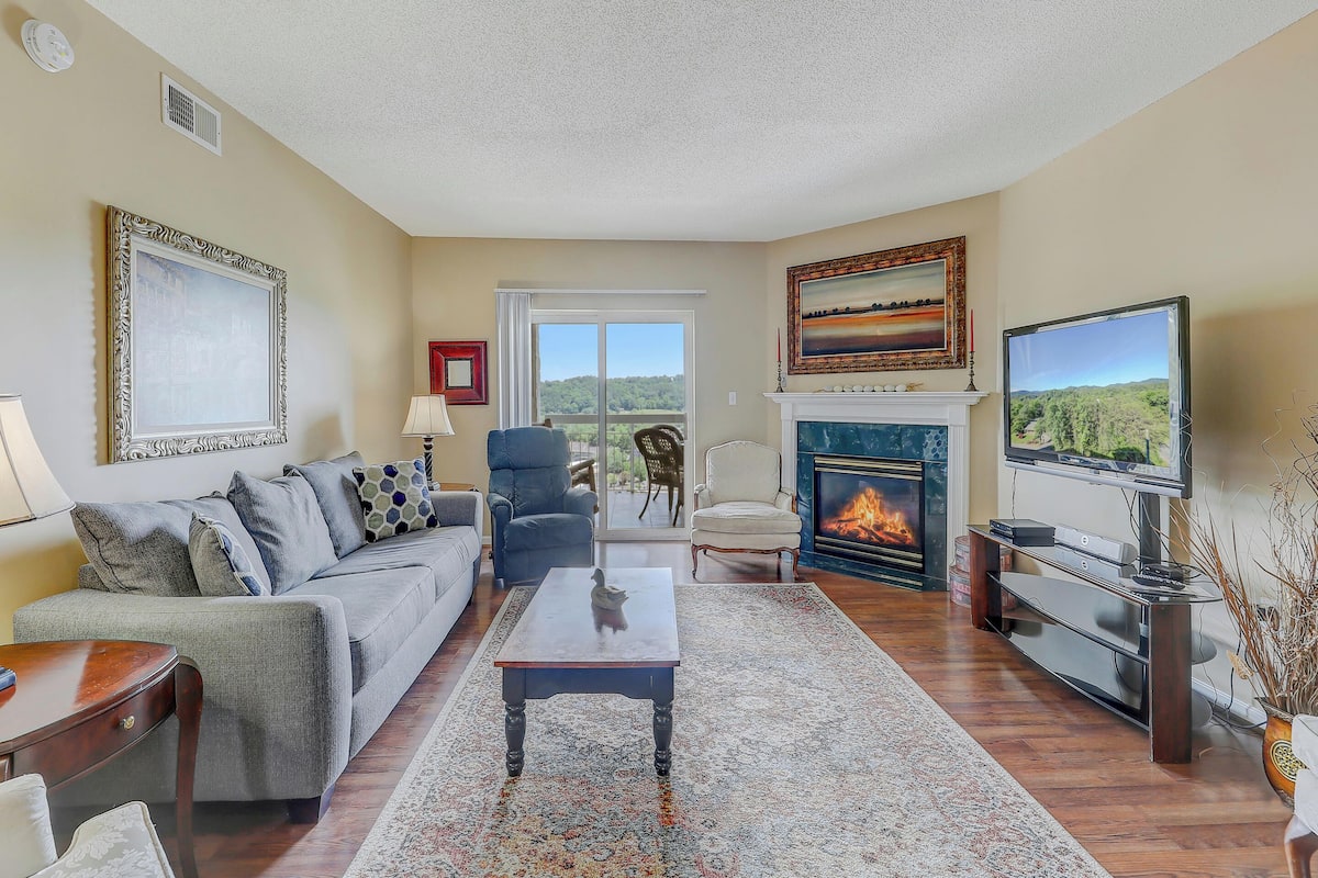 A living room with a sofa, armchairs, a fireplace, a television, and a view through a sliding glass door.