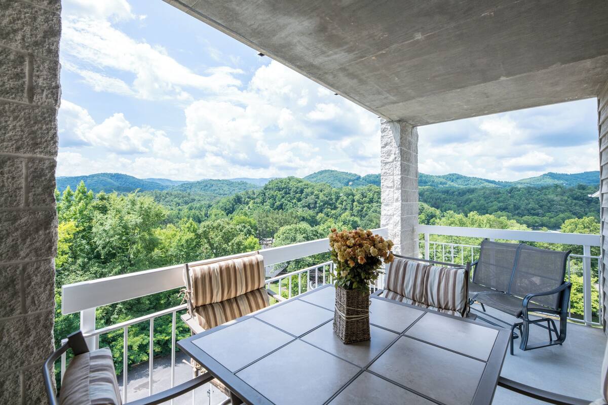 A balcony with a table, chairs, and a vase of flowers.