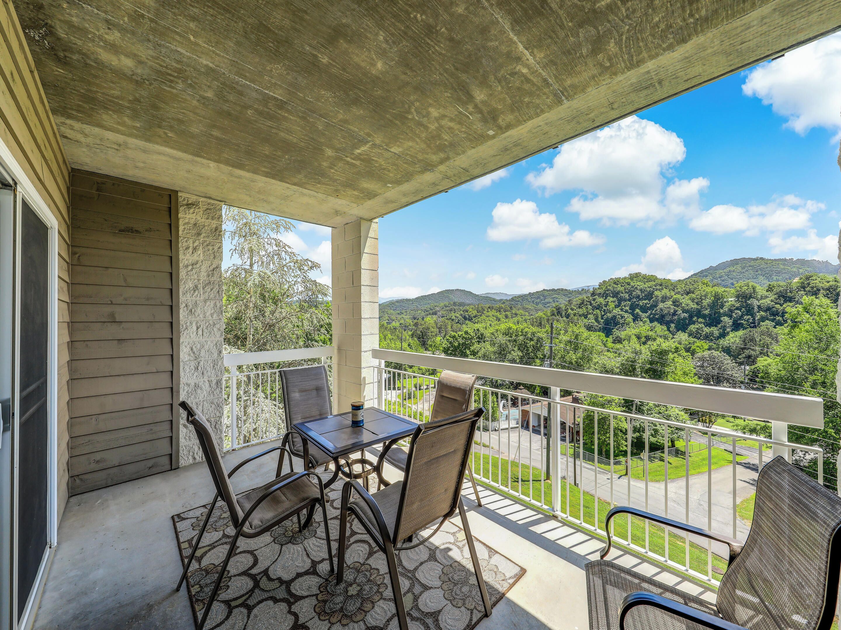 A balcony with a table and chairs, overlooking a lush green landscape and hills.