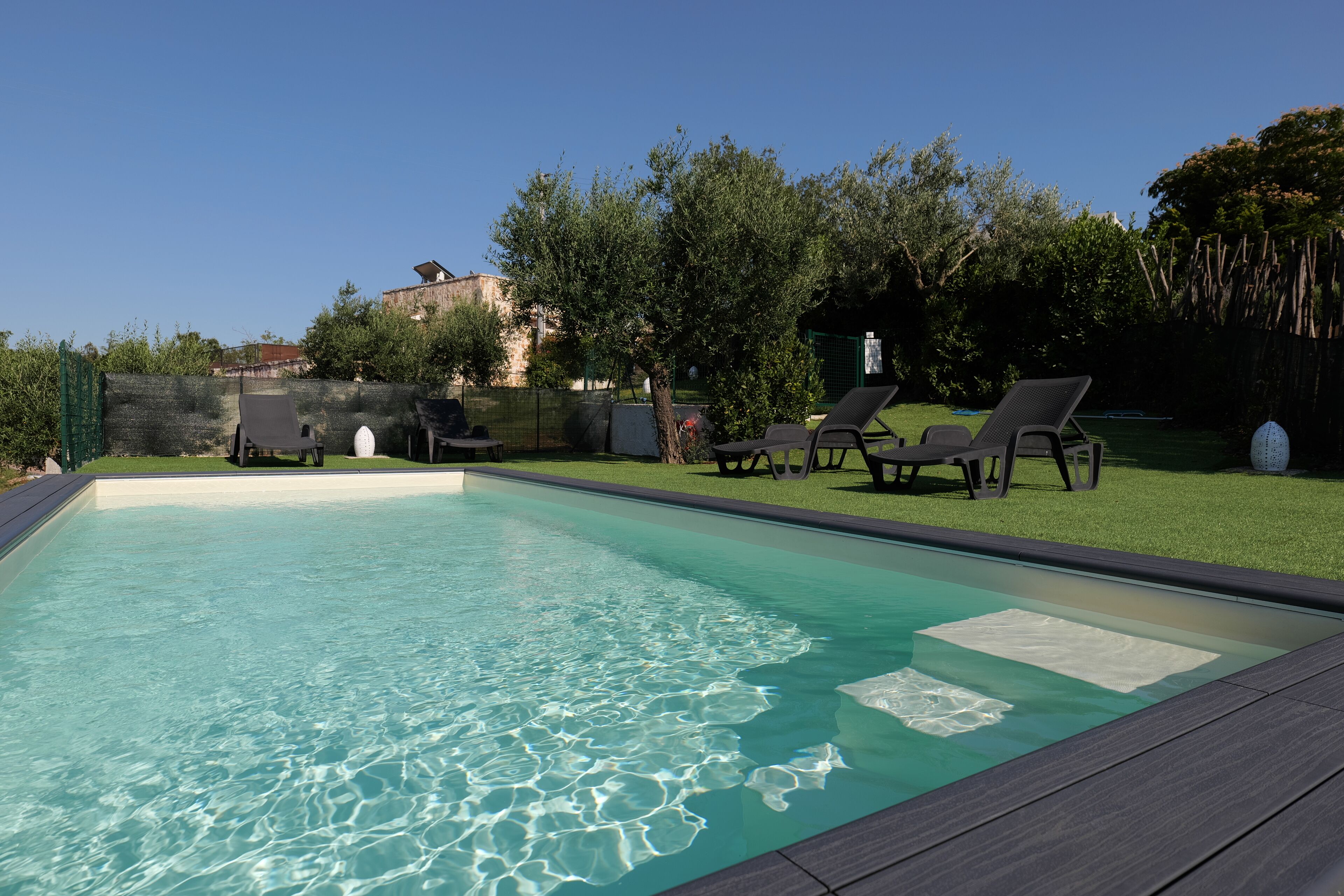 A rectangular swimming pool with clear water, surrounded by a wooden deck and a grassy area with lounge chairs.