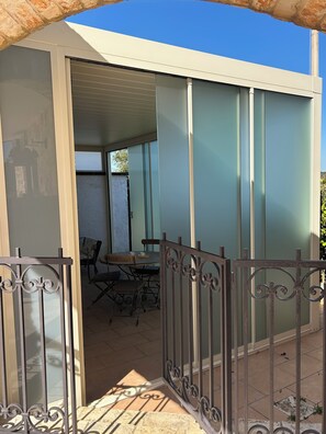 Un patio con mesa y sillas, una reja metálica y vistas al interior.