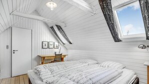 Une chambre avec un plafond en pente, un lit avec une couette à rayures, un bureau avec une chaise et une fenêtre avec des rideaux.