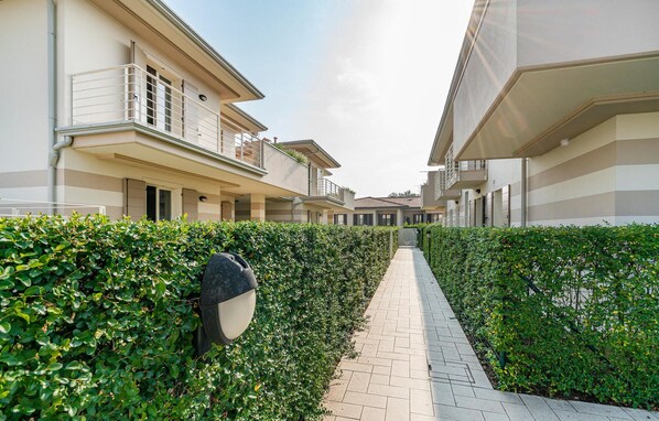A residential building with a paved walkway, a hedge, and a mailbox.