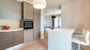 Una cocina moderna con electrodomésticos integrados, un comedor con una mesa y sillas blancas, y un ventanal que proporciona luz natural.