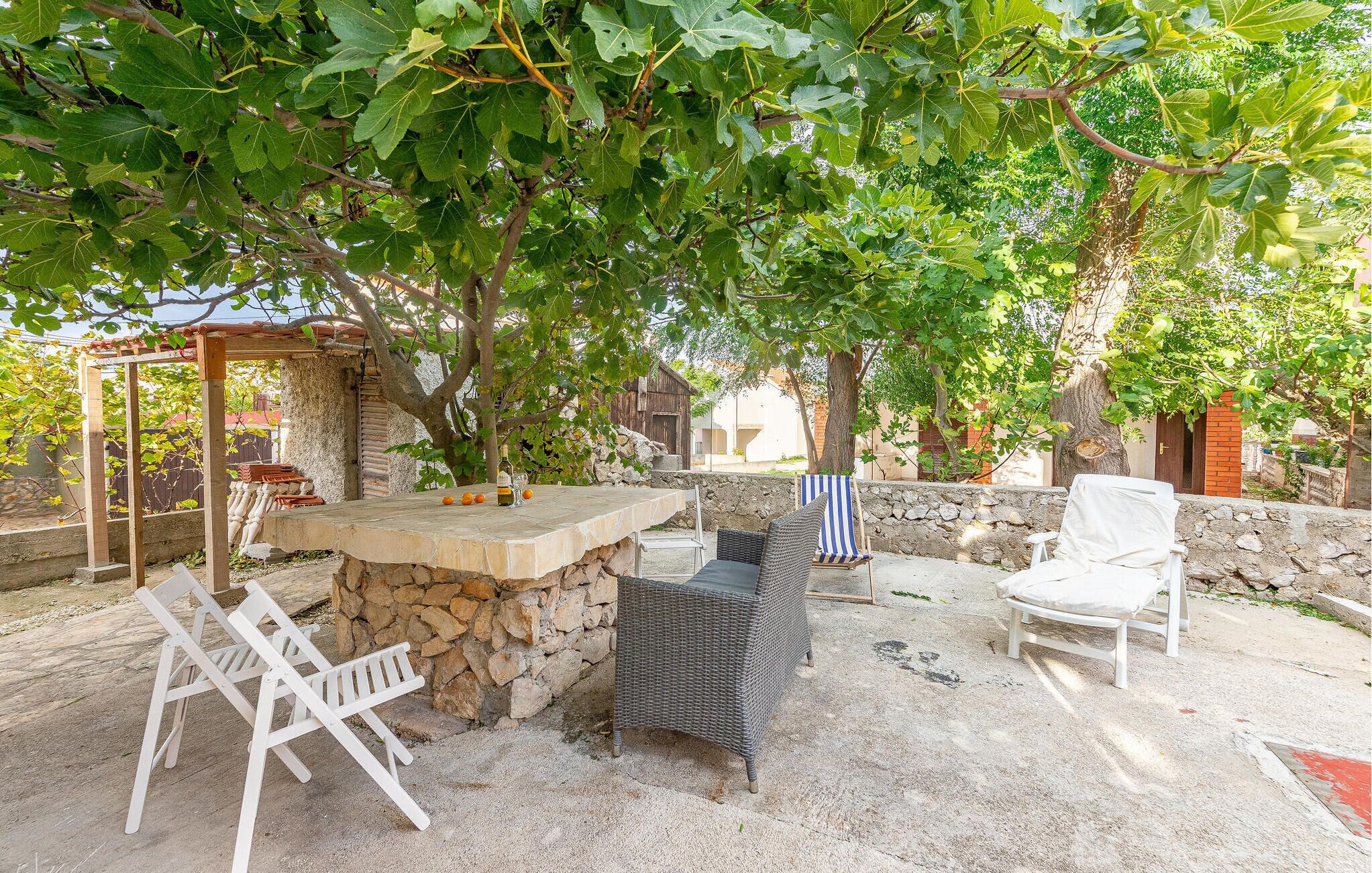 An outdoor patio with a stone table, wicker chairs, and a covered seating area under a tree.