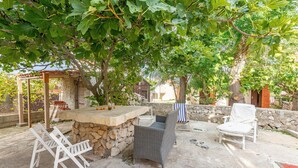 An outdoor patio with a stone table, wicker chairs, and a covered seating area under a tree. - Stunning apartment in Vir with WiFi (Vir)