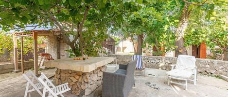 An outdoor patio with a stone table, wicker chairs, and a covered seating area under a tree.