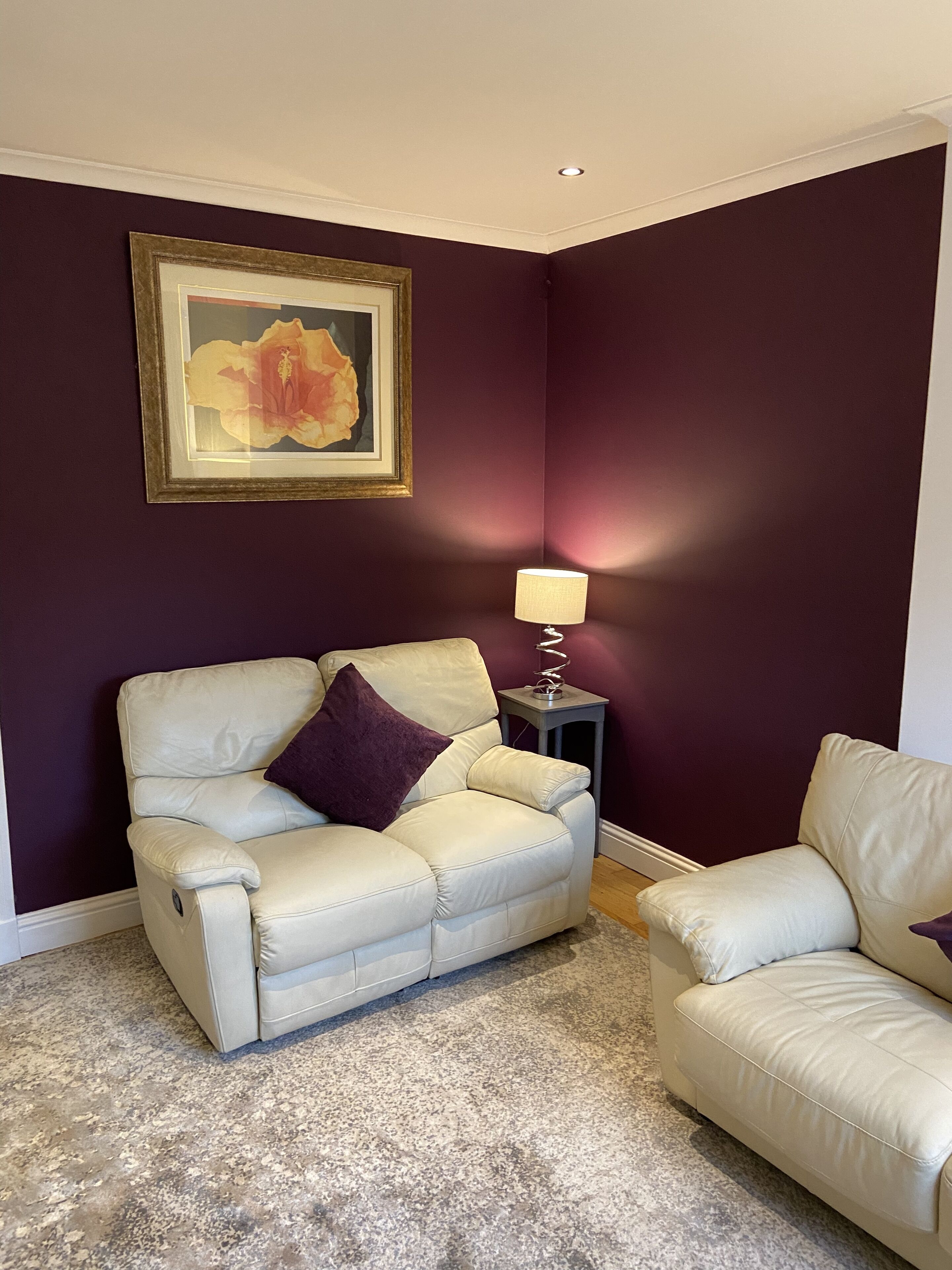Una sala de estar con un sofá color crema, una mesita auxiliar con una lámpara y una obra de arte enmarcada en la pared.