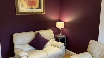 Una sala de estar con un sofá color crema, una mesita auxiliar con una lámpara y una obra de arte enmarcada en la pared.