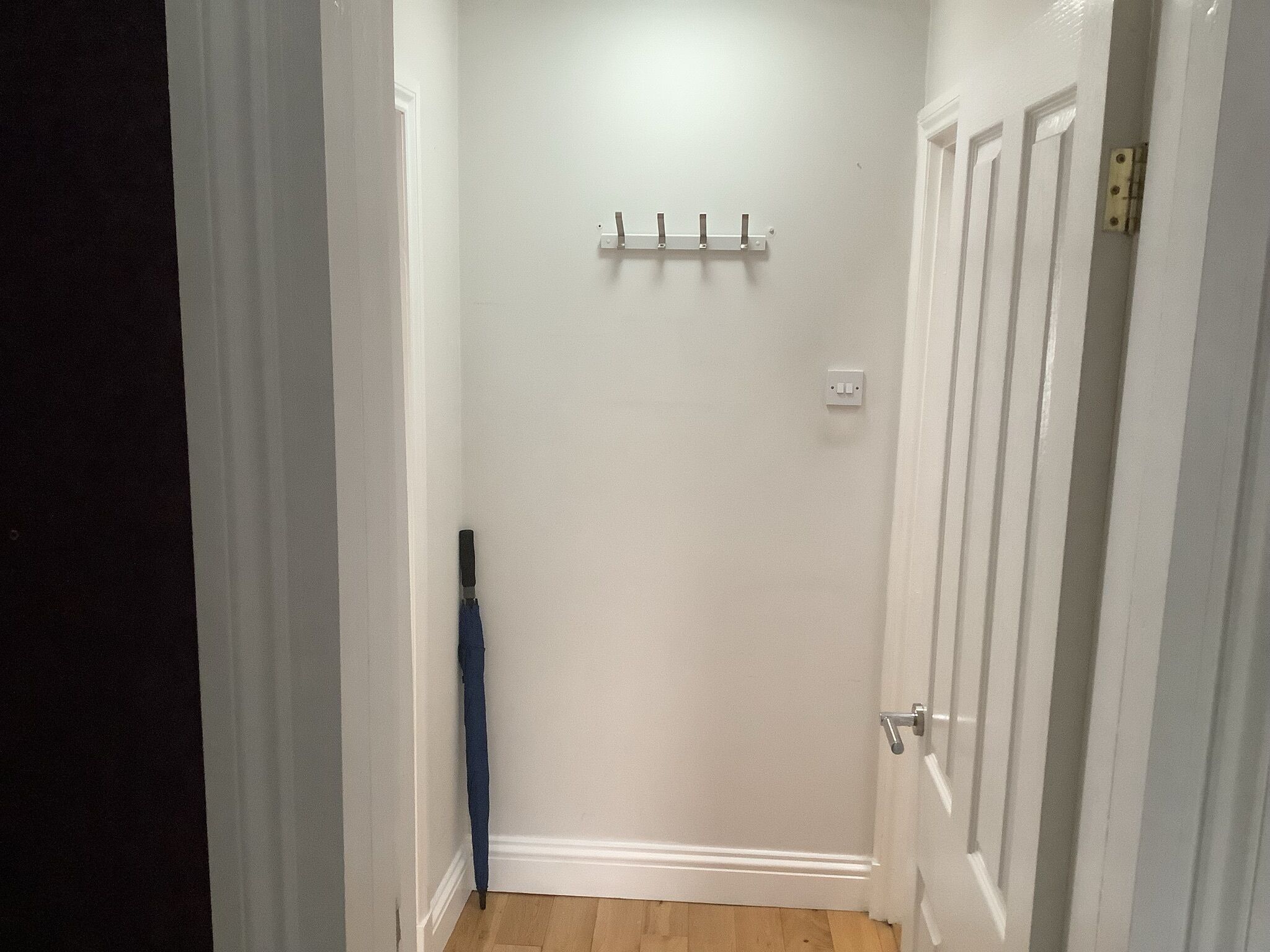 A narrow hallway with a wooden floor, a coat rack with hooks, and a door with a handle.