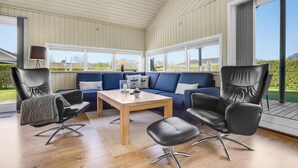 Et solbelyst rum med en blå sofa, to sorte læderstole, et træbord og en lampe.