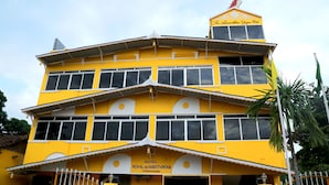 Un immeuble à plusieurs étages, doté d’une façade jaune, d’une enseigne indiquant « Hôtel Royal Sri Amirthanayoga Thirukondanadur » et d’un style architectural traditionnel.
