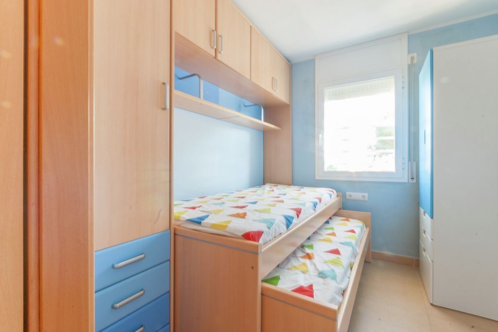 A bedroom with a bunk bed, wooden wardrobe, and a window with blinds.