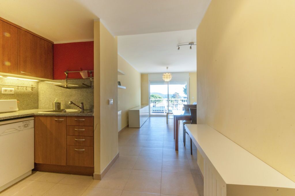 A modern kitchen with wooden cabinets, a built-in dishwasher, and a dining area with a table and chairs.