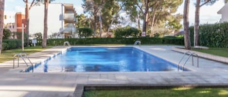 A rectangular swimming pool with two ladders on each side, surrounded by a paved deck and grass.