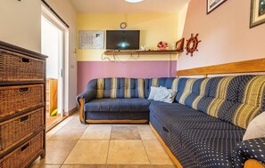 A cozy living room with a blue patterned sofa, wicker storage units, a television, and a wall clock. - Awesome apartment in Vir with WiFi (Vir)