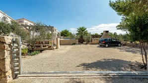 A courtyard with a gravel ground, a stone wall, a wooden pergola, and a car parked near a stone structure. - Awesome apartment in Vir with WiFi (Vir)
