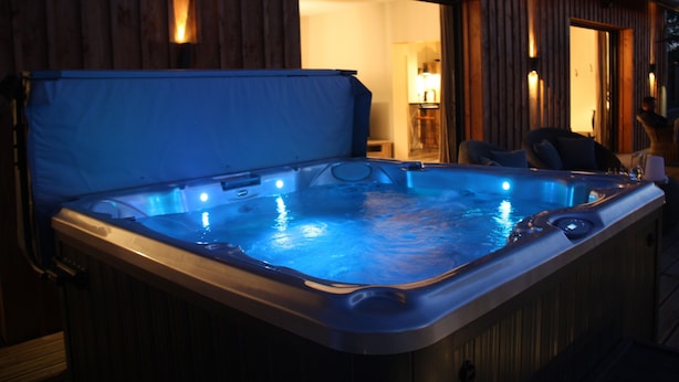 Ein Whirlpool mit blauer Abdeckung, Holzverkleidung und einem sichtbaren Eingang zu einem Innenbereich.