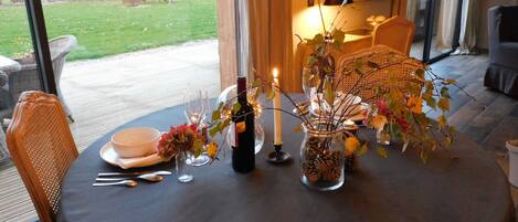A dining table set for two with a candle, a bottle of wine, and a vase with autumn leaves.