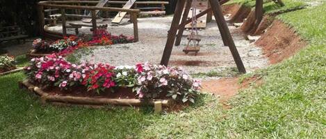 A playground with wooden structures, a swing set, and a flower bed.