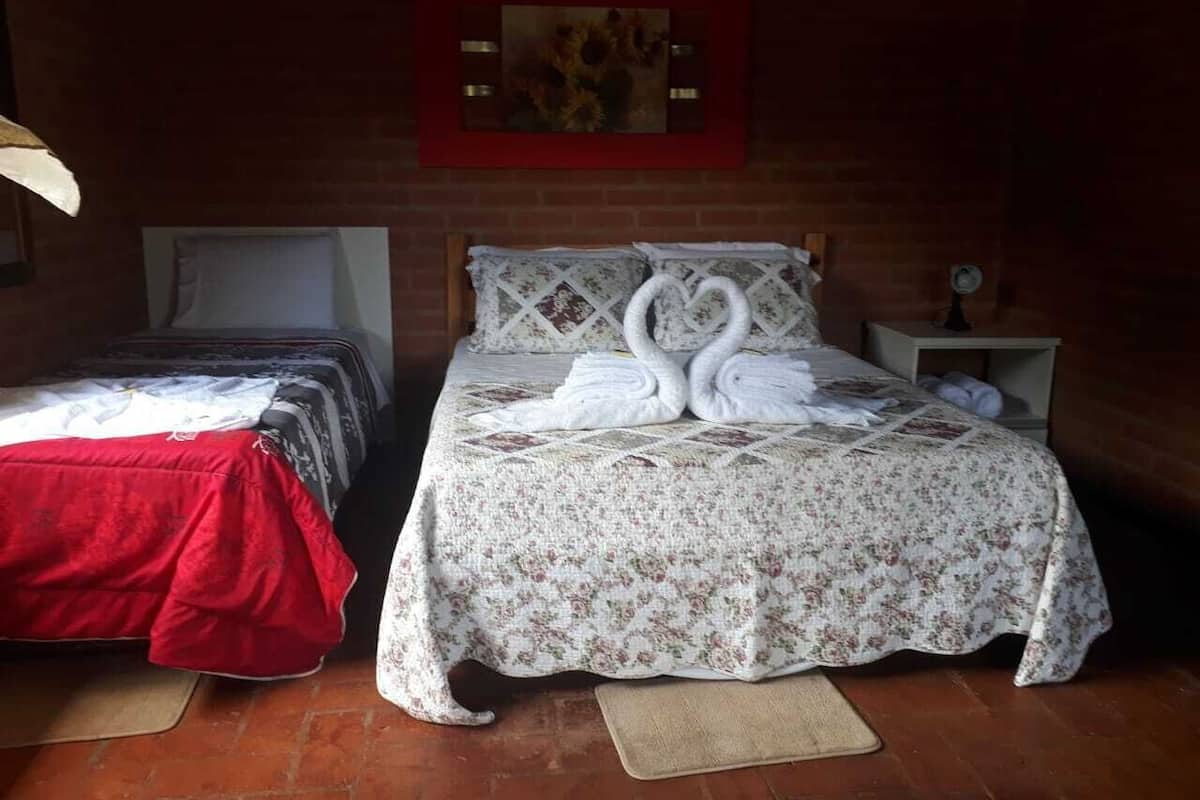 Zwei Betten mit Blumenmuster auf der Bettwäsche, eine rote Decke auf einem Bett, und eine Wanduhr auf der rechten Seite.