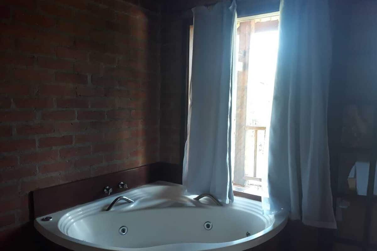 Ein Badezimmer mit Badewanne, einem Fenster mit Vorhängen und einer Ziegelwand.