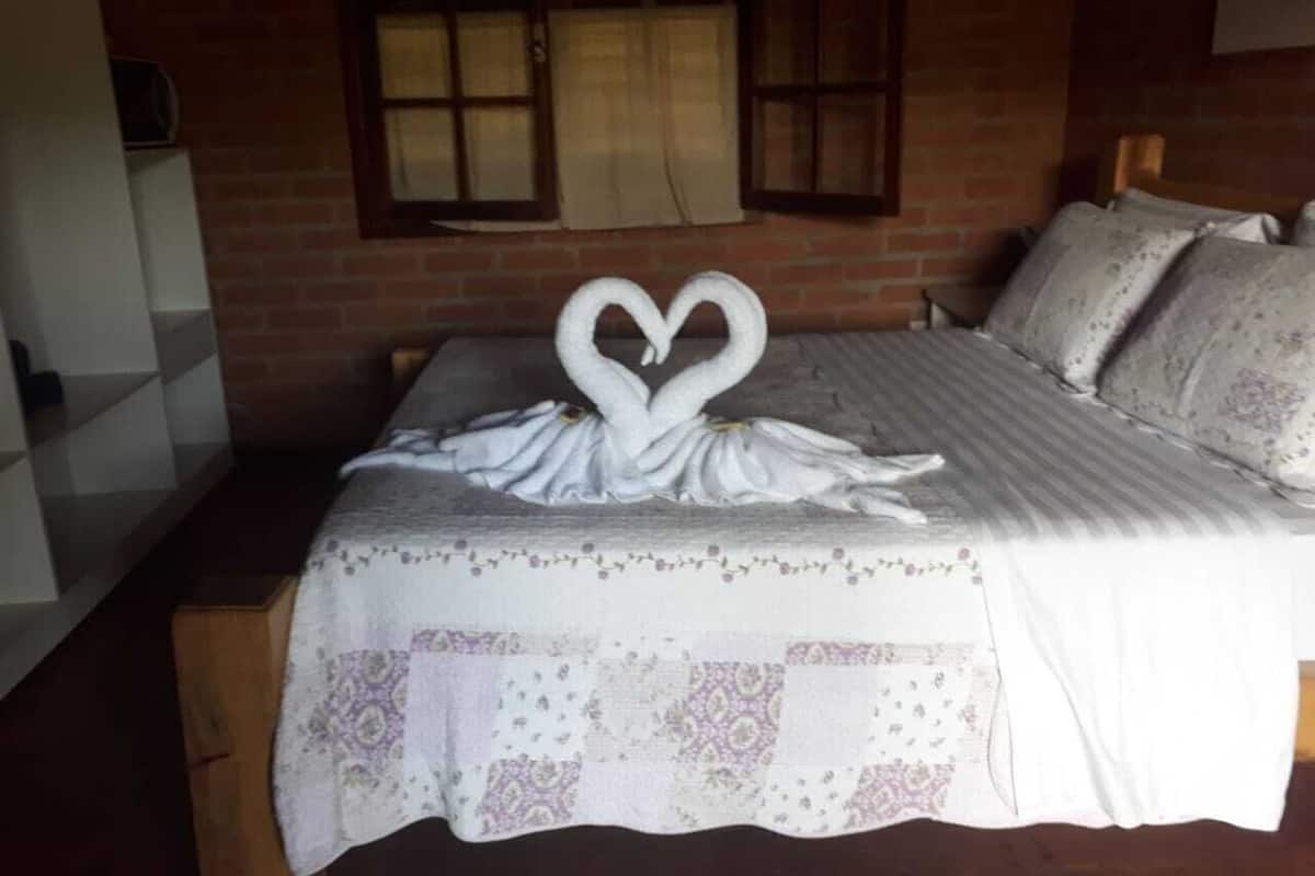 Ein Bett mit einer herzenförmigen Handtuchgestaltung, einer gemusterten Bettdecke und einer Ziegelwand mit Fenstern.